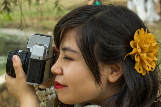 戴黄色花朵装饰长发女性举相机拍照