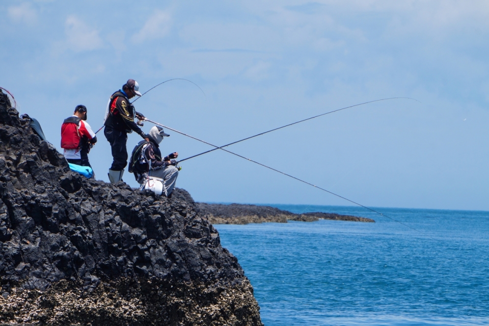 蓝色大海边岩石鱼竿钓鱼运动游人
