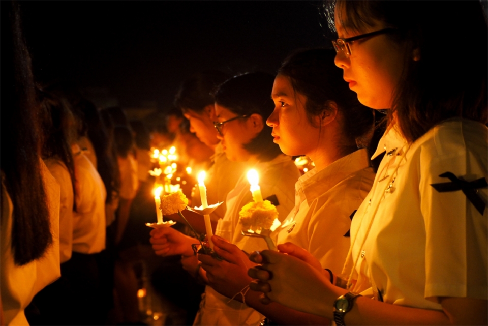 夜色下手捧着白色菊花和蜡烛正在哀悼的学生们