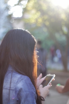 背景虚化阳光下玩手机的长发少女