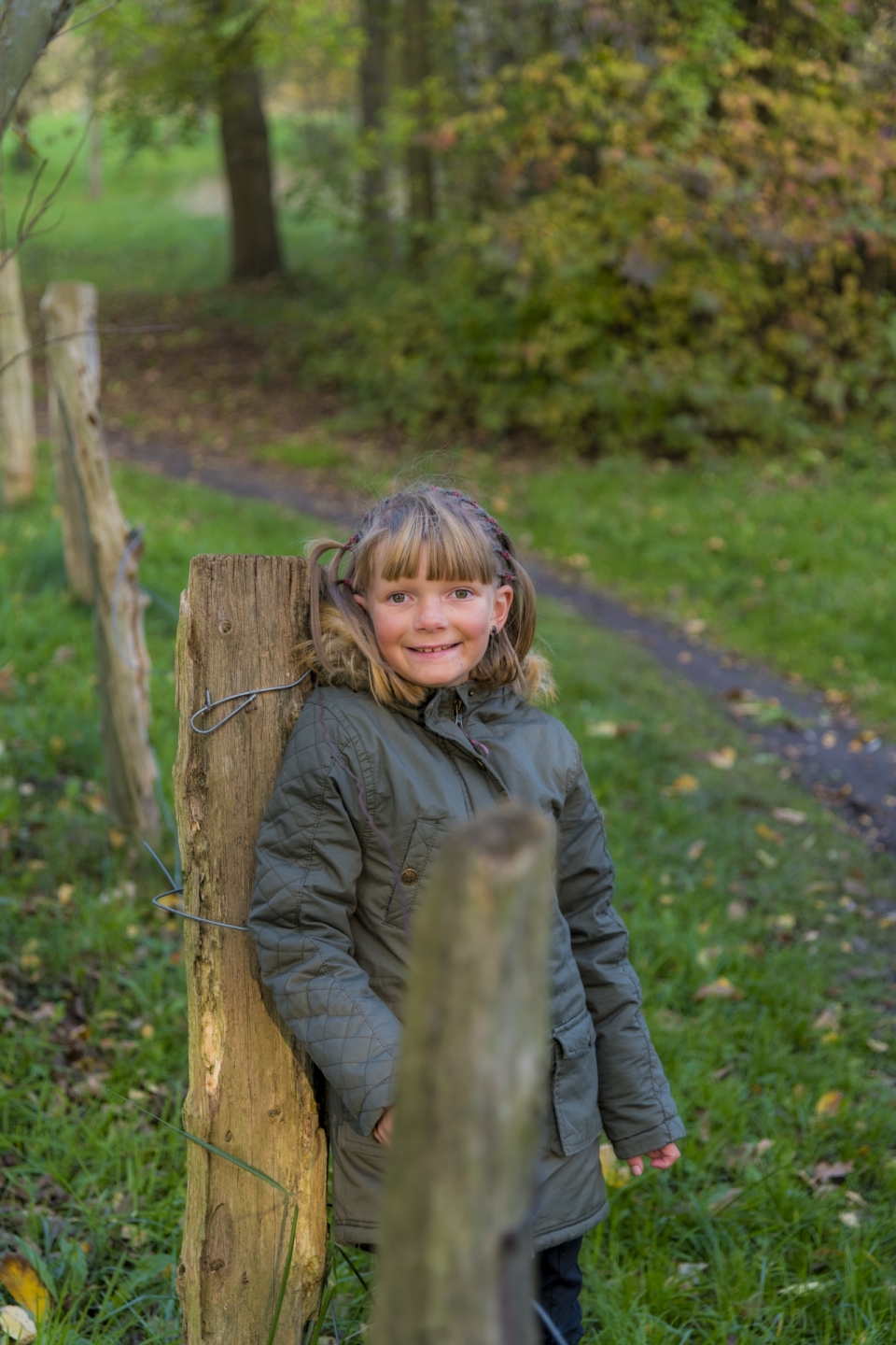 绿色树林小道草地旁靠在木桩上的小女孩