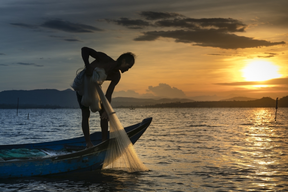 日落海面渔船中拉起渔网的渔民
