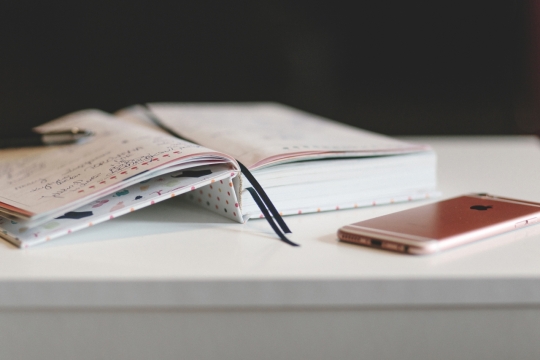 白色桌子上放着硬壳笔记本和苹果手机