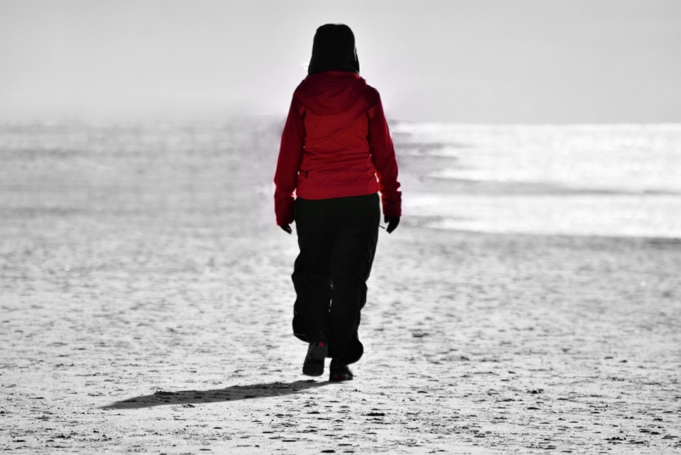 在黑白大海沙滩散步的红色外套女性背影
