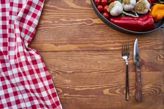 木桌上放着的刀叉、红白桌布和盛满食材的铁盘