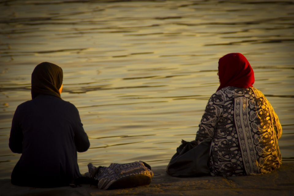 傍晚的夕阳下两个坐在河边草地上的妇女