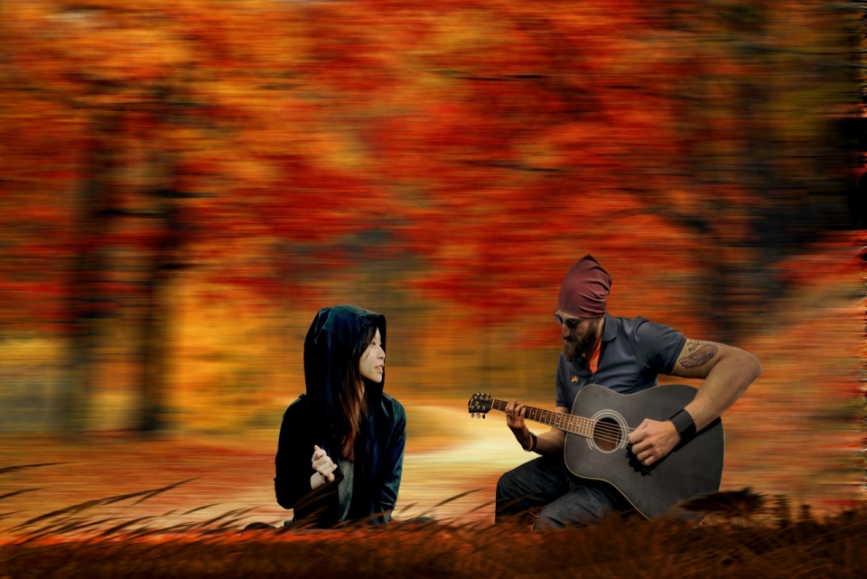 红色枫树林前弹吉他男子和戴帽子女子