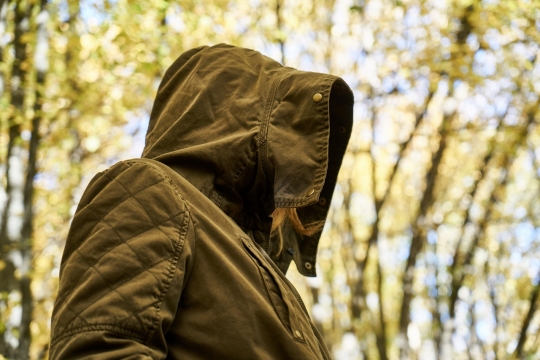 阳光下的树林中穿着大衣带着兜帽的人