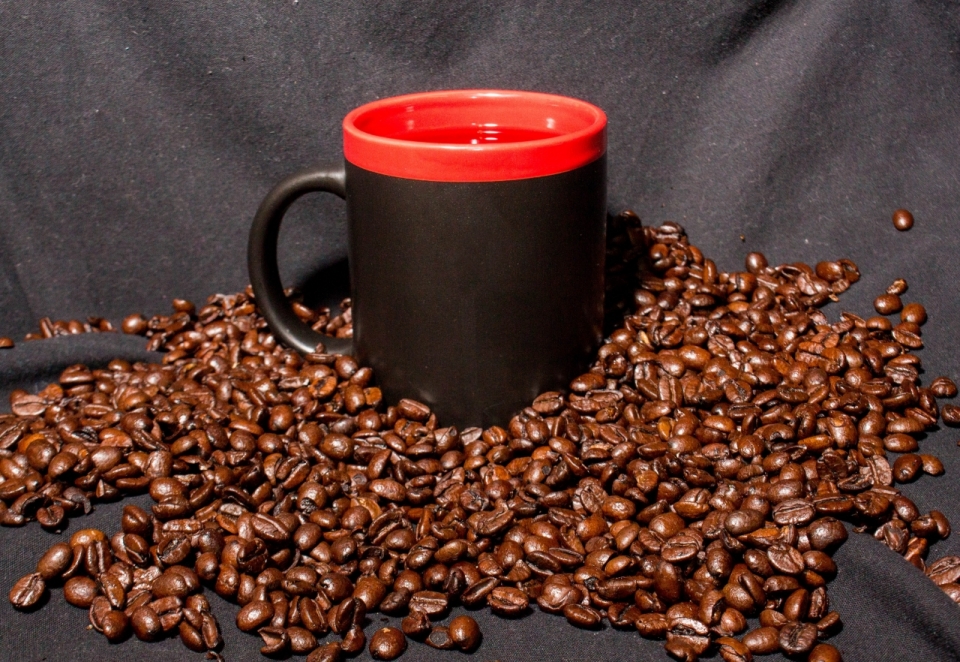 漆黑桌布上堆放烘烤油亮咖啡豆水杯