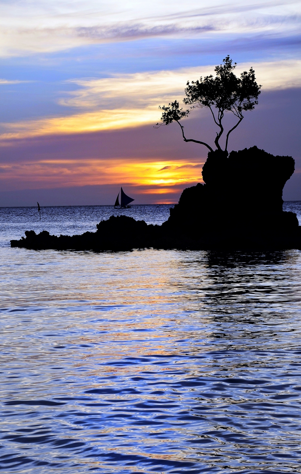 夕阳下海上礁石边的小帆船