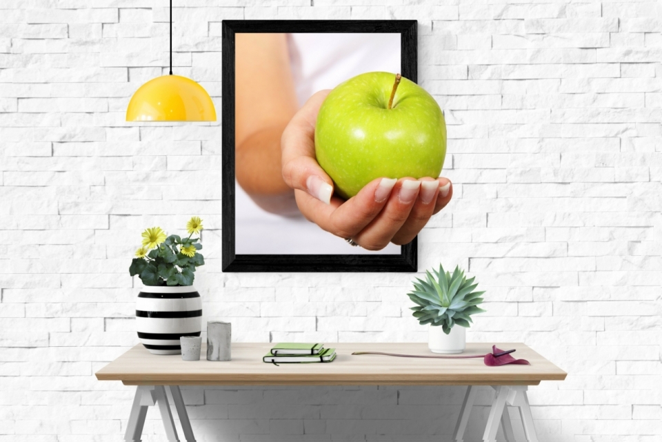 白色墙面画框中伸出一只握着绿色苹果的手
