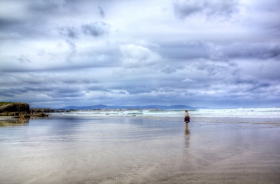 站在海边沙滩看翻滚海浪的游人