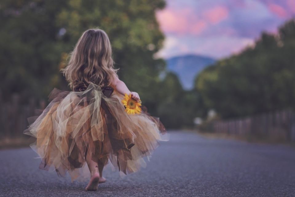 长裙小女孩手拿向日葵赤脚走在路上背影